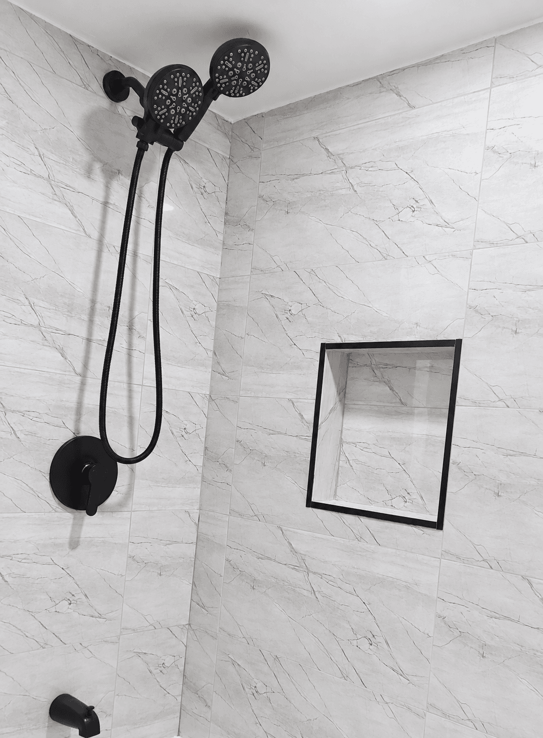 Shower wall tile, a recessed niche and black fixtures